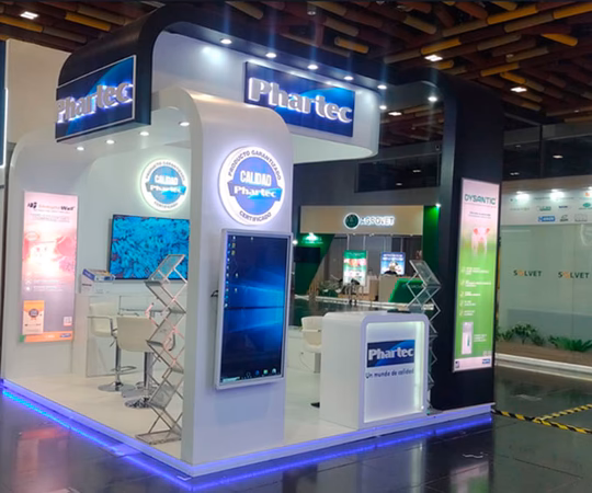 Moderno stand de exposición para PharTec con señalización luminosa, pantallas de visualización, carteles informativos y zona de asientos en un centro de convenciones.