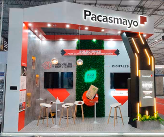 Stand de exposición de Pacasmayo con diseño moderno, expositores de productos, pantallas digitales y zona de asientos, en el que se muestran soluciones para el sector de la construcción en un evento.