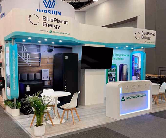 Stand de feria para BluePlanet Energy e Innovacion Solar con una mesa de exposición, sillas, plantas, una gran pantalla, imágenes de productos y gráficos informativos.